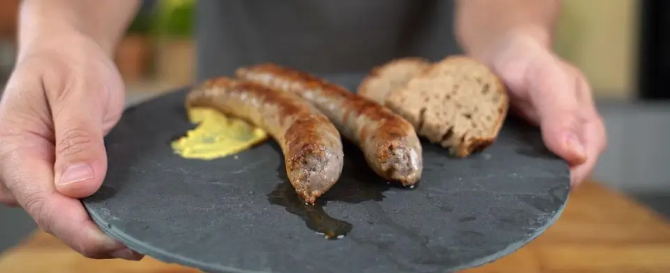 Two homemade Bratwurst, grilled and served on a slate plate with mustard and bread