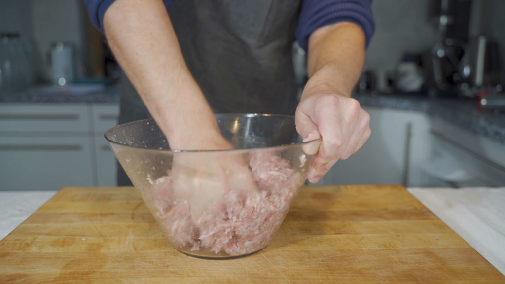 Mixing the sausage mixture vigorously to develop a good bind
